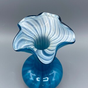 Puede incluir: Un jarr&oacute;n de vidrio azul con patrones de espiral blancos. El jarr&oacute;n tiene una abertura ancha y rizada y un cuerpo redondo.