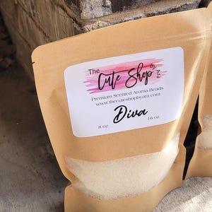 May include: A brown paper bag with a clear window, filled with white aroma beads. The bag has a label with the text "The Cute Shop" and "Diva". The label also includes the text "Premium Scented Aroma Beads" and "8 oz."
