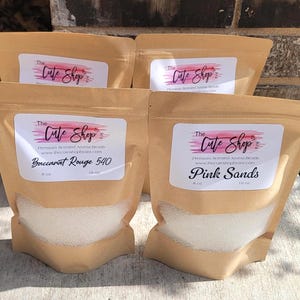 May include: Four brown paper bags filled with white beads. Each bag has a label that reads "The Cute Shop" and the product name. One bag is labeled "Baccarat Rouge 540" and another "Pink Sands".