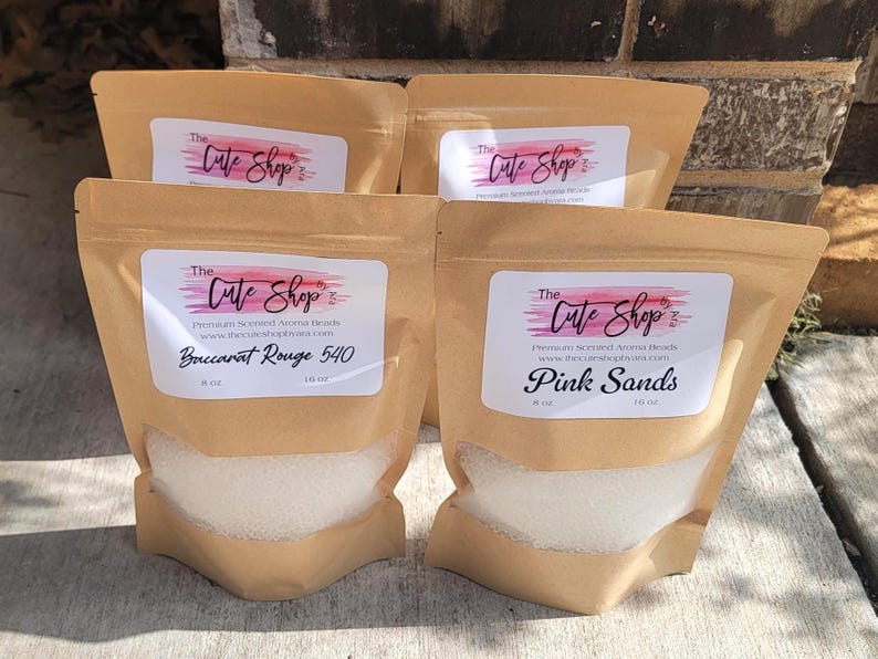 May include: Four brown paper bags filled with white beads. Each bag has a label that reads "The Cute Shop" and the product name. One bag is labeled "Baccarat Rouge 540" and another "Pink Sands".