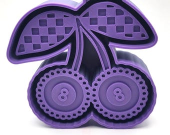 May include: A purple plastic cherry-shaped cookie cutter. The design includes checkered patterns on the leaves, dotted edges, and the number 8 inside the cherry halves. The cutter is designed for baking.