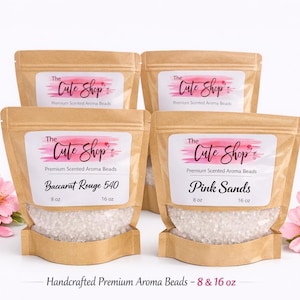 May include: Four kraft paper pouches of scented aroma beads, labeled "The Cute Shop." Two pouches are labeled "Baccarat Rouge 540" and "Pink Sands." Each pouch contains 8 or 16 oz of beads. Pink flowers are arranged around the pouches.
