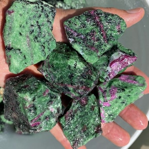 Peut inclure: Une collection de pierres précieuses de zoïsite brutes, vertes et roses. Les pierres ont des formes et des tailles variées, et elles sont toutes très brillantes.