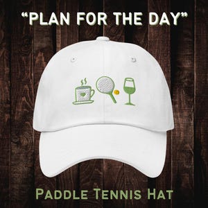 May include: White baseball cap with green embroidery of a coffee cup, paddle tennis racket, tennis ball, and wine glass. The text "PLAN FOR THE DAY" is above the cap and "PADDLE TENNIS HAT" is below the cap.
