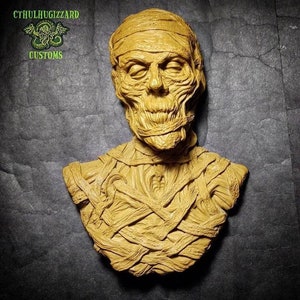 May include: A detailed bust sculpture of a mummy, with a realistic depiction of the face and body wrapped in bandages. The sculpture is painted in a light brown color, giving it a realistic appearance.