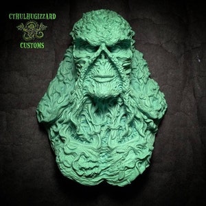 May include: A green, detailed, sculpted bust of a creature with a humanoid face and a textured, plant-like body. The bust is against a dark gray background. The text "CTHULHUGIZZARD CUSTOMS" is in the top left corner of the image.