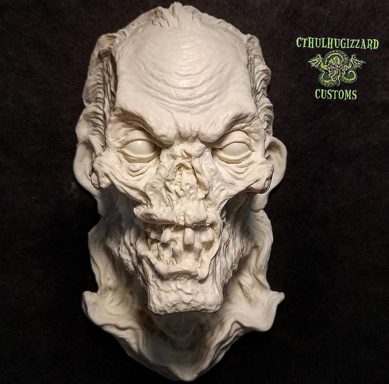 K&ouml;nnte beinhalten: Eine wei&szlig;e Gips-Skulptur eines Zombiekopfes mit einem bedrohlichen Ausdruck. Die Skulptur ist detailliert mit Falten und Z&auml;hnen. Die Skulptur ist signiert mit "CTHULHUGIZZARD CUSTOMS".