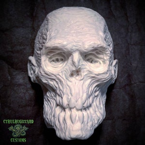 May include: A white, detailed, sculpted human skull with a grotesque, toothy grin. The skull is made of a smooth, white material and has a textured surface.
