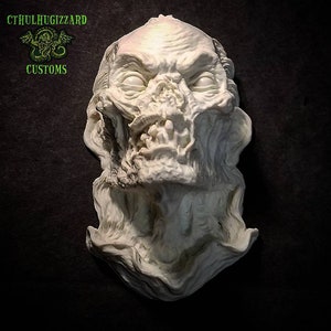 K&ouml;nnte beinhalten: Ein wei&szlig;er, detaillierter, geformter Kopf eines Monsters mit einem gro&szlig;en Maul und scharfen Z&auml;hnen. Die Skulptur befindet sich auf einem dunklen Hintergrund. Der Text "CTHULHUGIZZARD CUSTOMS" befindet sich in der oberen linken Ecke des Bildes.
