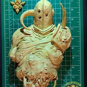 May include: A detailed, light-tan sculpture of a creature with a helmet-like head, multiple holes, and a textured body. The sculpture has a horn-like appendage and a shield-like element. A small, ornate piece and the "CTHULHUGIZZARD CUSTOMS" logo are also visible.