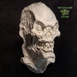 K&ouml;nnte beinhalten: Eine wei&szlig;e Gips-Skulptur eines Zombiekopfes mit einem detaillierten, grotesken Ausdruck. Die Skulptur ist auf einem Sockel montiert und hat eine strukturierte Oberfl&auml;che.
