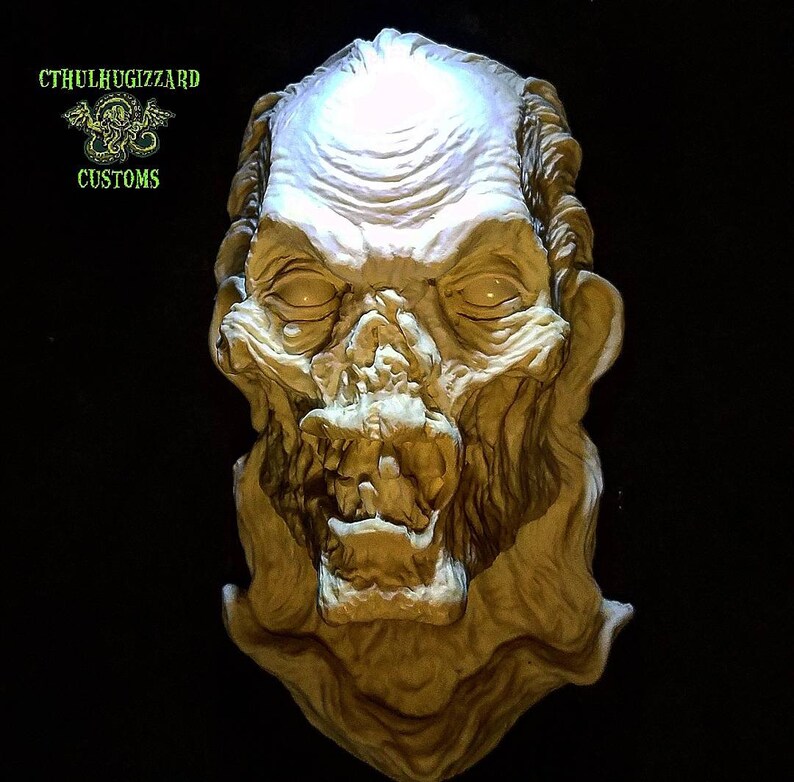 K&ouml;nnte beinhalten: Eine detaillierte, handbemalte, wei&szlig;e Gips-Skulptur eines monstr&ouml;sen, skelettartigen Gesichts mit einem aufgerissenen Mund und einer strukturierten, faltigen Oberfl&auml;che. Die Skulptur wird von oben beleuchtet, wodurch die filigranen Details hervorgehoben werden.
