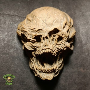 May include: A detailed, textured, brown, sculpted skull with a wide open mouth and rows of teeth. The skull is made of a smooth, hard material and has a realistic appearance.