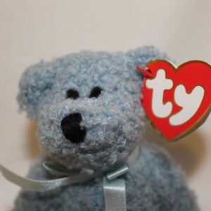 May include: A blue fuzzy beanie baby with a black nose and a red and white Ty tag.