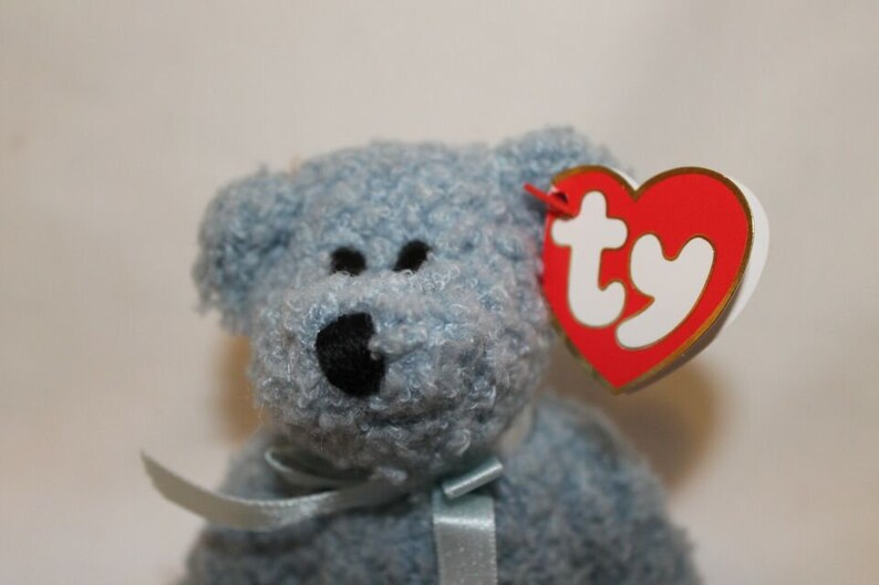 May include: A blue fuzzy beanie baby with a black nose and a red and white Ty tag.