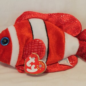 May include: Red and white plush clownfish beanie baby toy with a blue eye and a Ty tag that says "Beanie Baby".