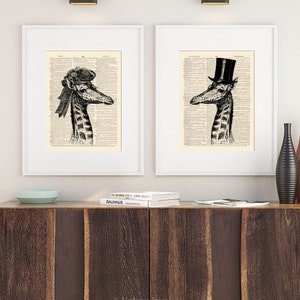 May include: Two framed black and white illustrations of giraffes wearing hats. The giraffe on the left is wearing a black and white hat with a ribbon. The giraffe on the right is wearing a black top hat. Both illustrations are printed on a vintage dictionary page background.