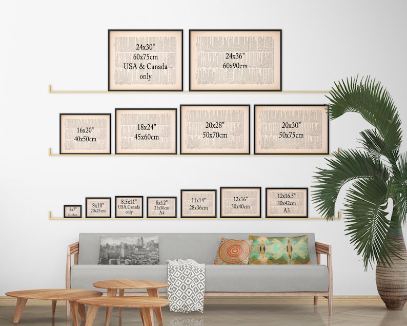 May include: A white wall with a shelf displaying various sizes of framed black and white prints. The prints are all of the same design, a vintage newspaper article. The sizes are listed in inches and centimeters. The shelf is made of wood and is mounted on the wall. There is a gray couch with pillows in front of the shelf. The couch is in a living room setting with a green plant and a coffee table.