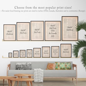 May include: A white wall with a variety of framed prints in different sizes. The prints are all black and white and feature text. The prints are arranged in a grid pattern. The wall is also decorated with a green plant and a couch with pillows.