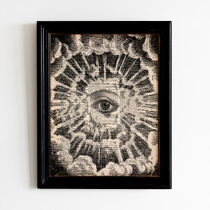 May include: A black and white print of an eye surrounded by a burst of light and clouds. The print is framed in a black frame.