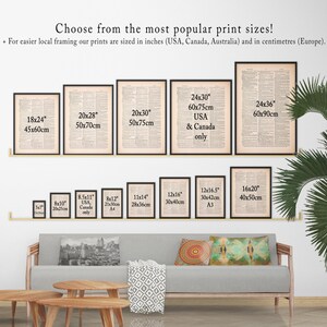 May include: A white wall with a variety of framed prints in different sizes. The prints are all black and white and feature text. The prints are arranged in a grid pattern. The wall is also decorated with a green plant and a couch with pillows.