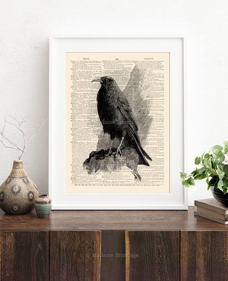 May include: A black and white illustration of a crow perched on a branch, printed on a vintage book page. The image is framed in a white frame.