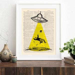 May include: A black and white illustration of a flying saucer hovering over a man in a suit and top hat. The saucer is emitting a yellow beam of light. The image is printed on a vintage dictionary page.