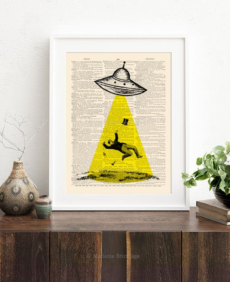 May include: A black and white illustration of a flying saucer hovering over a man in a suit and top hat. The saucer is emitting a yellow beam of light. The image is printed on a vintage dictionary page.