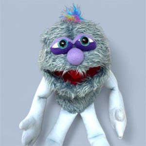 May include: A plush puppet with a shaggy, gray fur-like exterior. It features large, purple-rimmed eyes with black pupils, a purple nose, and a red mouth. The puppet has light blue arms and legs, and a tuft of rainbow-colored hair.