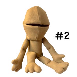 May include: A tan puppet with a large, open mouth and a rounded head. The puppet has arms and legs with detailed hands and feet. The number "#2" is printed in black on the right side of the puppet.