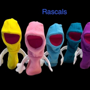 Puede incluir: Cinco pasamontañas de forro polar en amarillo, rosa, azul claro, azul cerceta y morado, cada uno con brazos de tela blanca con manos y un forro interior rosa oscuro. La palabra Rascals está impresa en azul sobre los artículos.