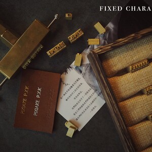 May include: A set of brass letter stamps in a wooden box with a burlap lining. The stamps are arranged in rows and are used for stamping leather or paper. The text "FIXED CHARACTER" is visible at the top of the image.
