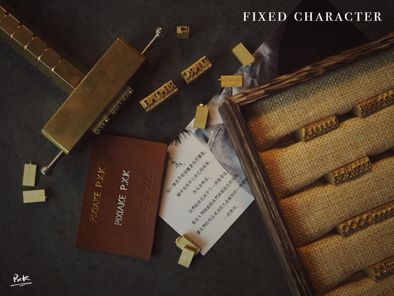 May include: A set of brass letter stamps in a wooden box with a burlap lining. The stamps are arranged in rows and are used for stamping leather or paper. The text "FIXED CHARACTER" is visible at the top of the image.