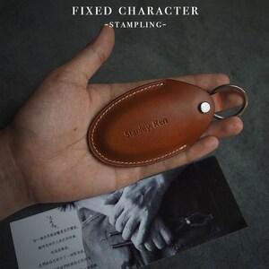 May include: A brown leather key fob with a stitched edge and a silver key ring. The fob is embossed with the text "Stanley. Ren".