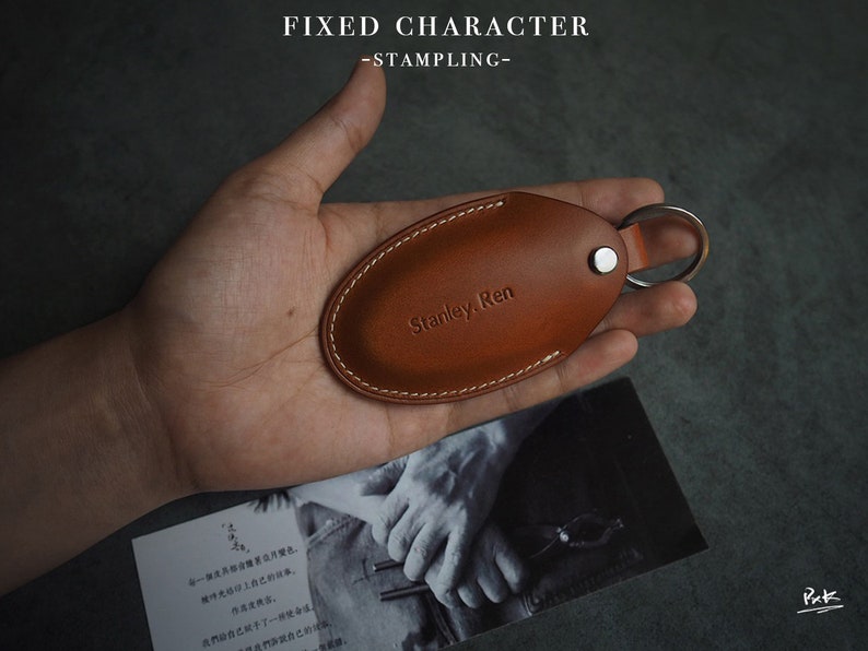 May include: A brown leather key fob with a stitched edge and a silver key ring. The fob is embossed with the text "Stanley. Ren".