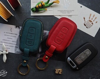 May include: Two leather key covers, one green and one red, with a black key fob. The key covers have a stitched edge and a metal ring for attaching to a keychain. The key fob has three buttons.