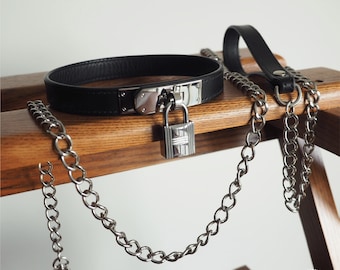 May include: A black leather choker with a silver lock and chain. The chain is attached to a leather handle.