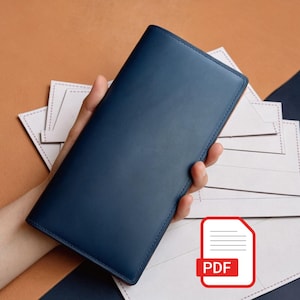 May include: A long, rectangular navy blue leather wallet with a smooth, matte finish. The wallet is held in a vertical position, showcasing its clean, minimalist exterior design and stitched edges. The item is presented against a background of white paper templates.