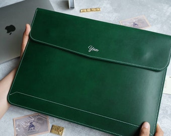 Könnte beinhalten: Eine dunkelgrüne Laptoptasche aus Leder mit weißen Nähten und dem Namen "Yuen" auf der Vorderseite gestickt.