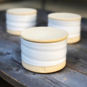 May include: Three white ceramic containers with lids. The containers have a ridged design and a light brown rim. The lids are a light brown color.