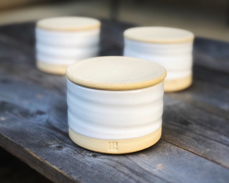 May include: Three white ceramic containers with lids. The containers have a ridged design and a light brown rim. The lids are a light brown color.