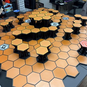 Può includere: Un set di terreno modulare per giochi da tavolo con tessere esagonali arancioni e piattaforme nere rialzate. Il layout presenta varie altezze e tessere specifiche contrassegnate con i numeri 1, 2, 4 e un simbolo rosso su una griglia.