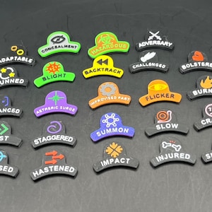 May include: A collection of black, curved game tokens with various colored text and icons. The tokens feature words like "Adaptable," "Stunned," and "Fast." The tokens are designed for tabletop gaming.