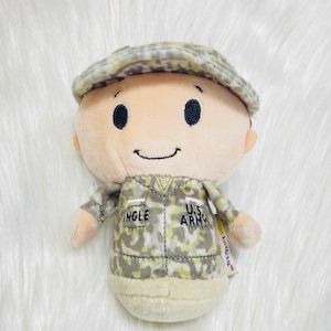 May include: A plush toy soldier with a camouflage uniform, a hat, and a smiling face. The uniform has the text "U.S. ARMY" and "INGLE" on it. The toy is made by the brand "1st & 10th".