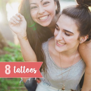 May include: Two women are smiling and laughing together outdoors. The woman in the front is wearing a grey tank top and jeans. The woman in the back is wearing a blue shirt and has a tattoo on her arm. The text "8 tattoos" is visible in the image.