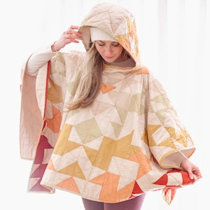 Könnte beinhalten: Gesteppter Poncho mit geometrischem Muster in Beige-, Orange- und Gelbtönen. Der Poncho hat eine Kapuze und ein kapuzenartiges Design. Das Kleidungsstück besteht aus weichem, gestepptem Material.