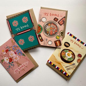 May include: Four greeting cards with kraft paper backing. The cards feature colorful illustrations, including floral bouquets and Korean food dishes. Each card has text in Korean. The cards are arranged on a white surface.