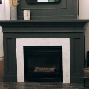 May include: A dark gray fireplace mantel with a white marble surround and a black fireplace insert. The fireplace is decorated with a white wicker candle holder.
