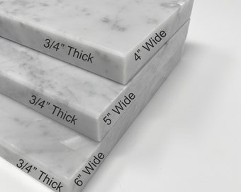 May include: Three white marble slabs stacked on top of each other. The slabs are 3/4 inch thick and 4, 5, and 6 inches wide.