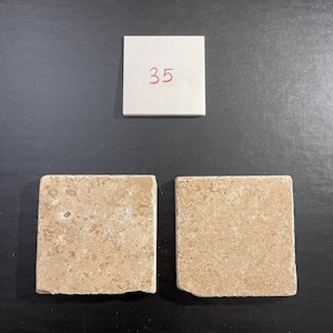 May include: Two beige square tiles with a rough texture. The tiles are numbered 35 on a white note.